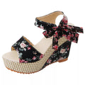 Gorgeous pair of espadrilles with cross-strap, floral print, and narrow wedge heel on sunlit tile floor