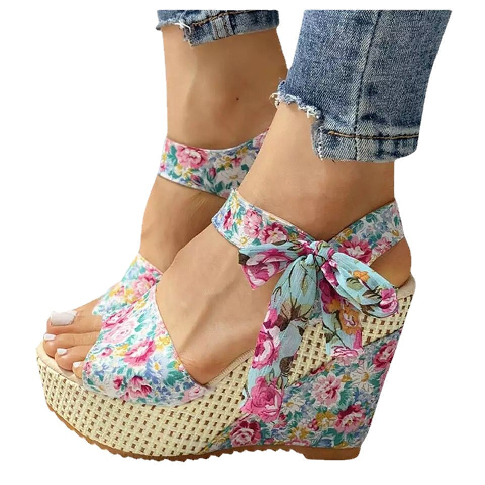 Gorgeous pair of espadrilles with cross-strap, floral print, and wedge heel on sunlit tile floor