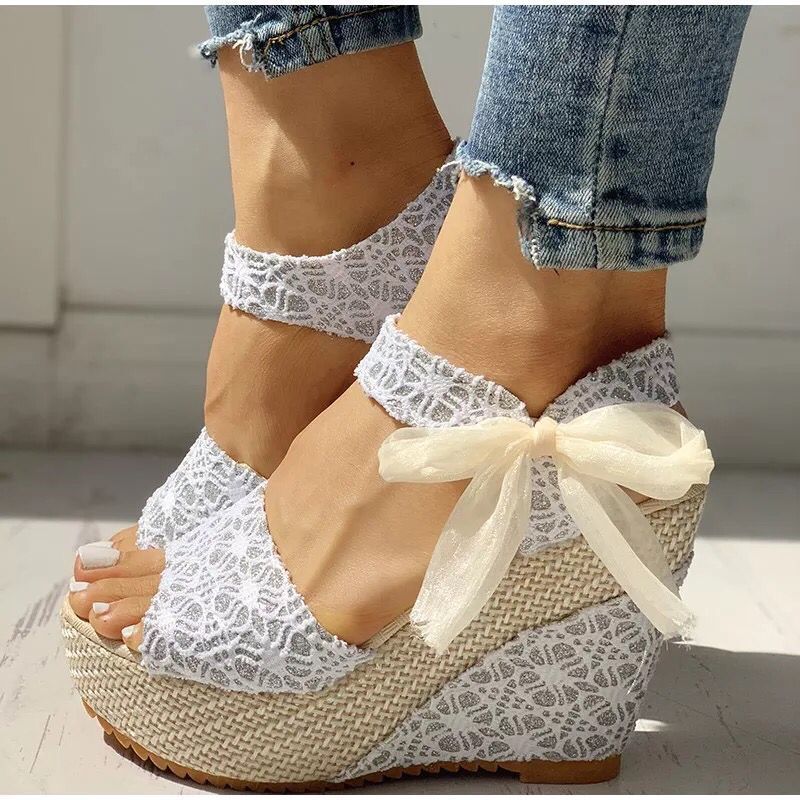 Gorgeous pair of espadrilles with satin ribbons, floral embroidery, and narrow wedge heel on sunlit tile floor