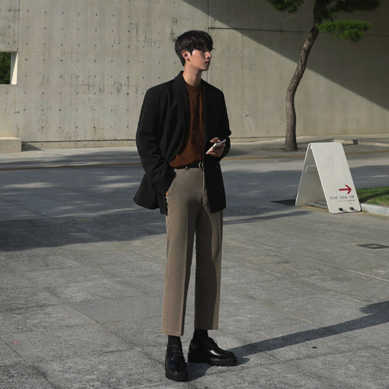 Tall male model wearing slim-fitting suit pants with low-rise cut and belt buckle, standing outdoors