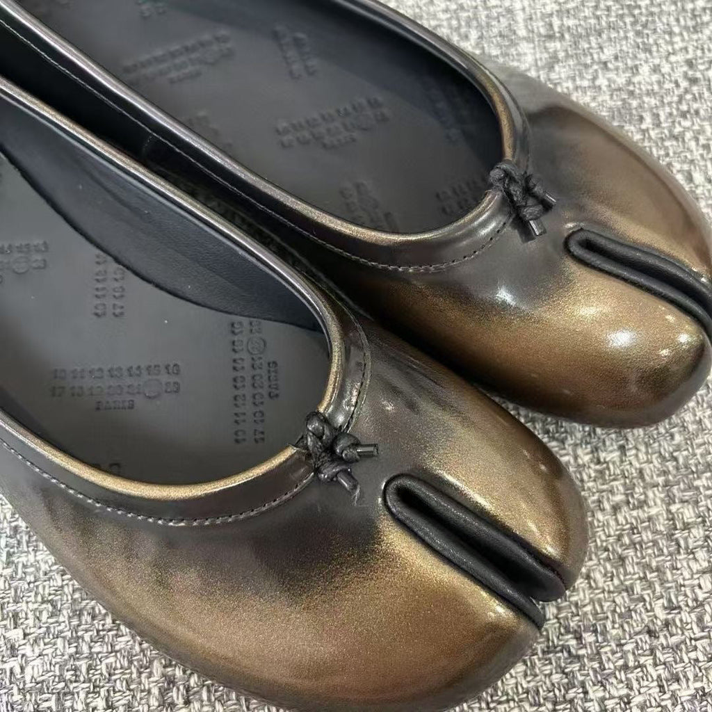 Close-up of gold and black vegan leather tabi shoes with split-toe design on concrete floor